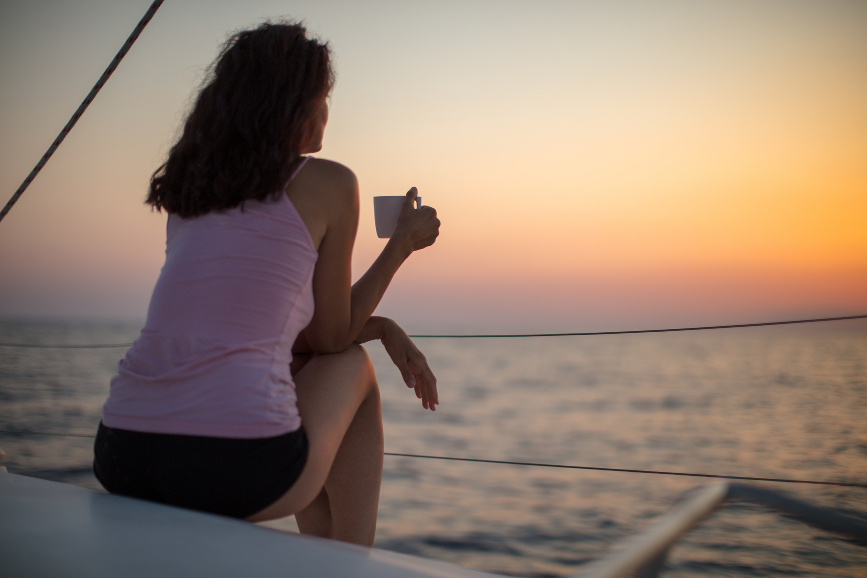 Woman drinking coffee at sunrise while sailing